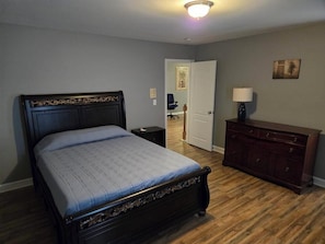 Een slaapkamer met een bed, een kaptafel, nachtkastje en een deur naar een andere kamer.