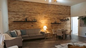 Una sala de estar con pared de ladrillo, un sofá, una mesa con sillas y una lámpara.