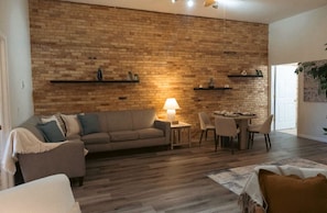 Una sala de estar con pared de ladrillo, un sofá, una mesa con sillas y una lámpara.