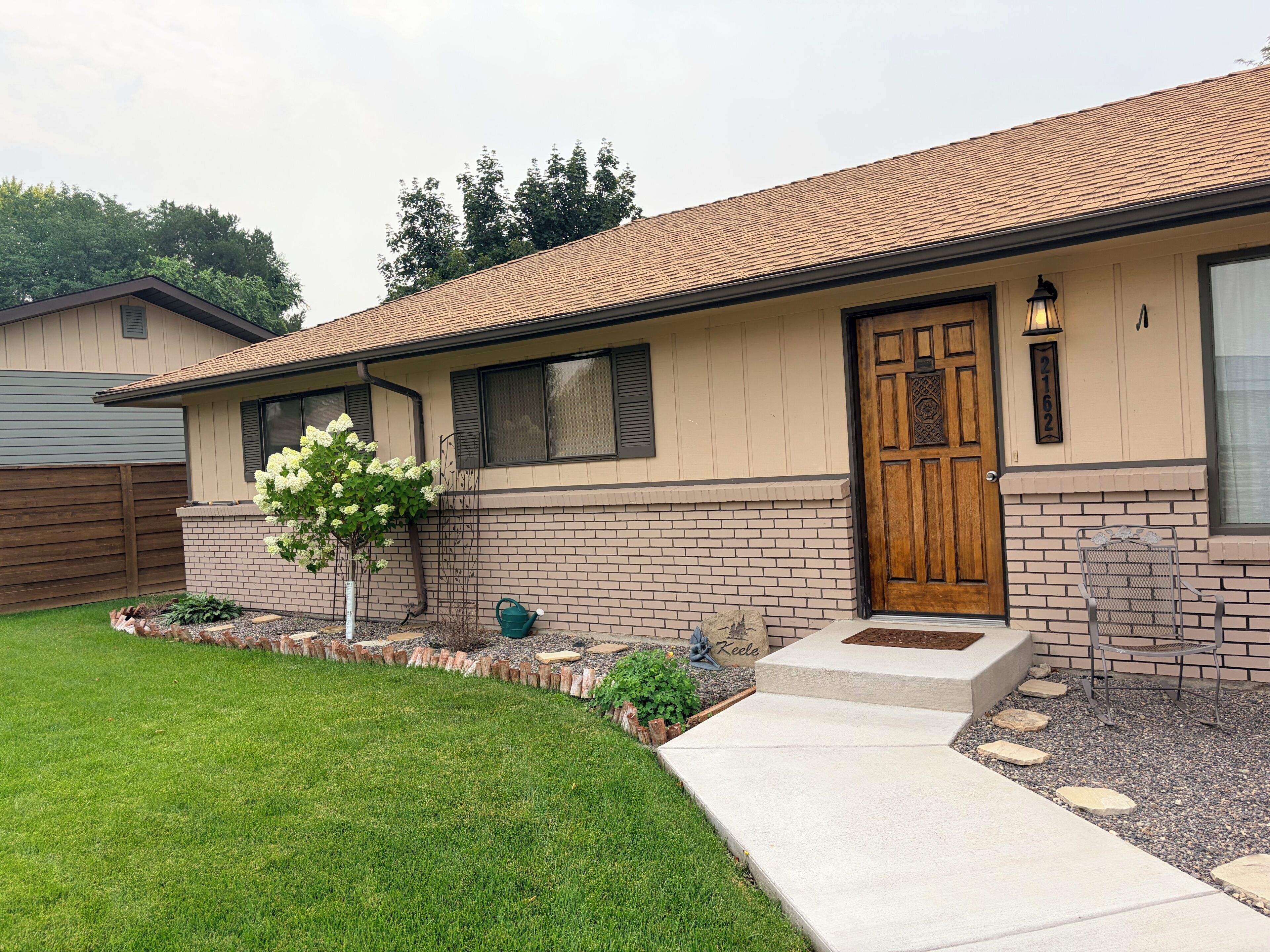 A single-story house with a brick facade, a wooden front door, and a small front yard with a tree and stepping stones.