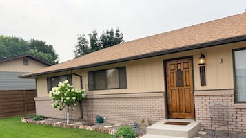 A single-story house with a brick facade, a wooden front door, and a small front yard with a tree and stepping stones.