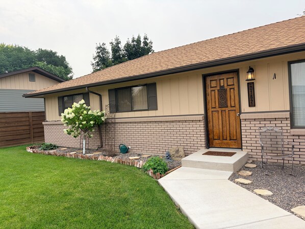 A single-story house with a brick facade, a wooden front door, and a small front yard with a tree and stepping stones.