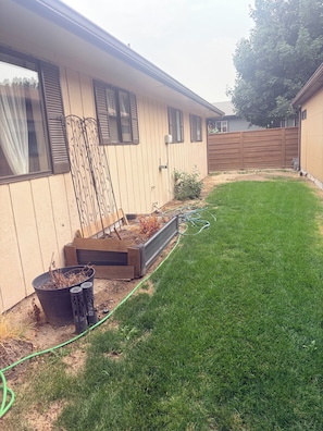 A residential backyard with a lawn, raised garden beds, a wooden fence, and a hose.