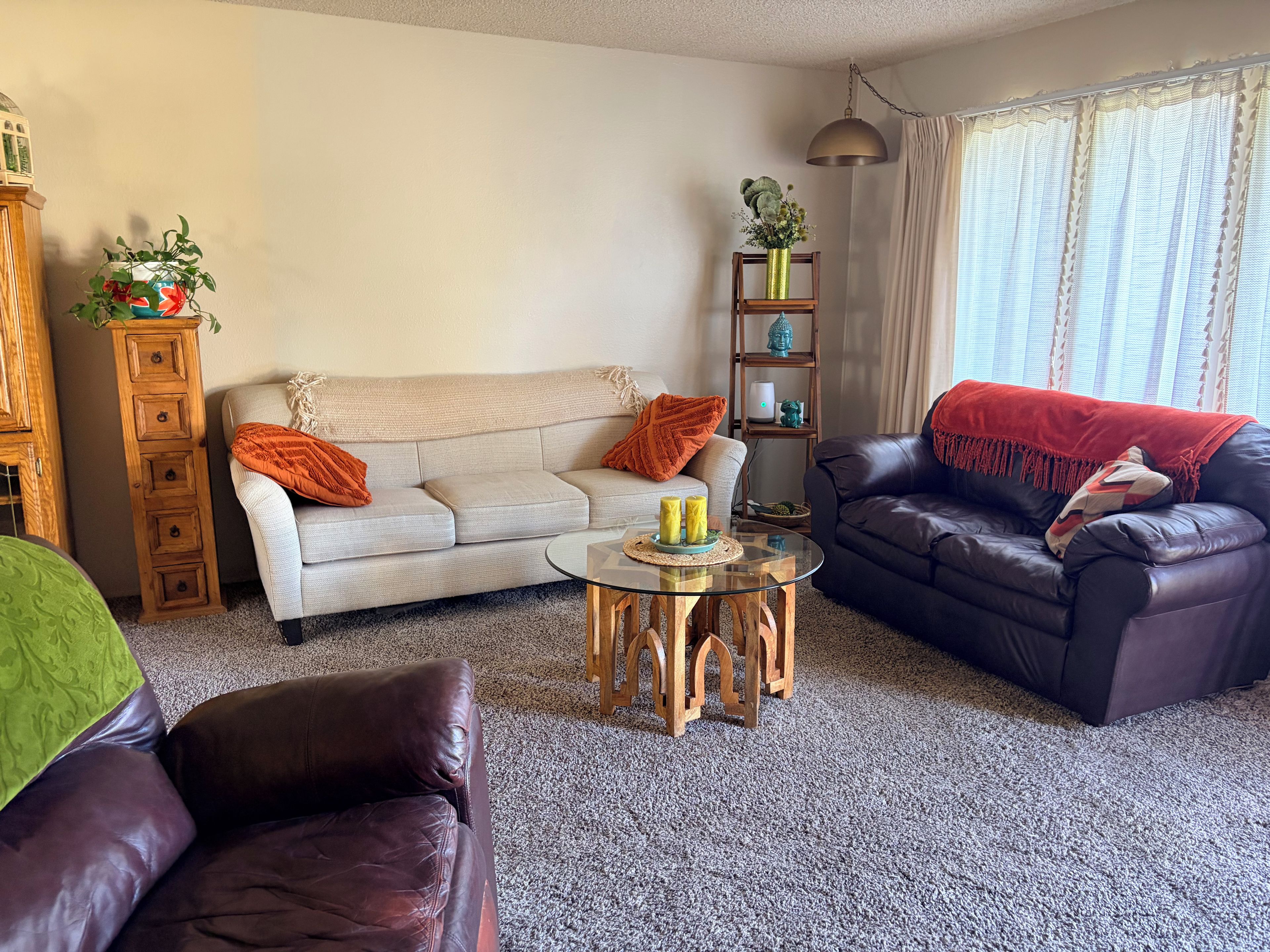 Un salon comprenant un canapé, une table basse, un divan en cuir foncé, un meuble en bois et une étagère ornée d’objets décoratifs.