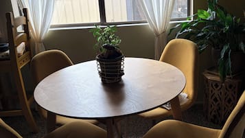 A room with a round wooden table, two yellow chairs, a potted plant, and a window with sheer curtains.