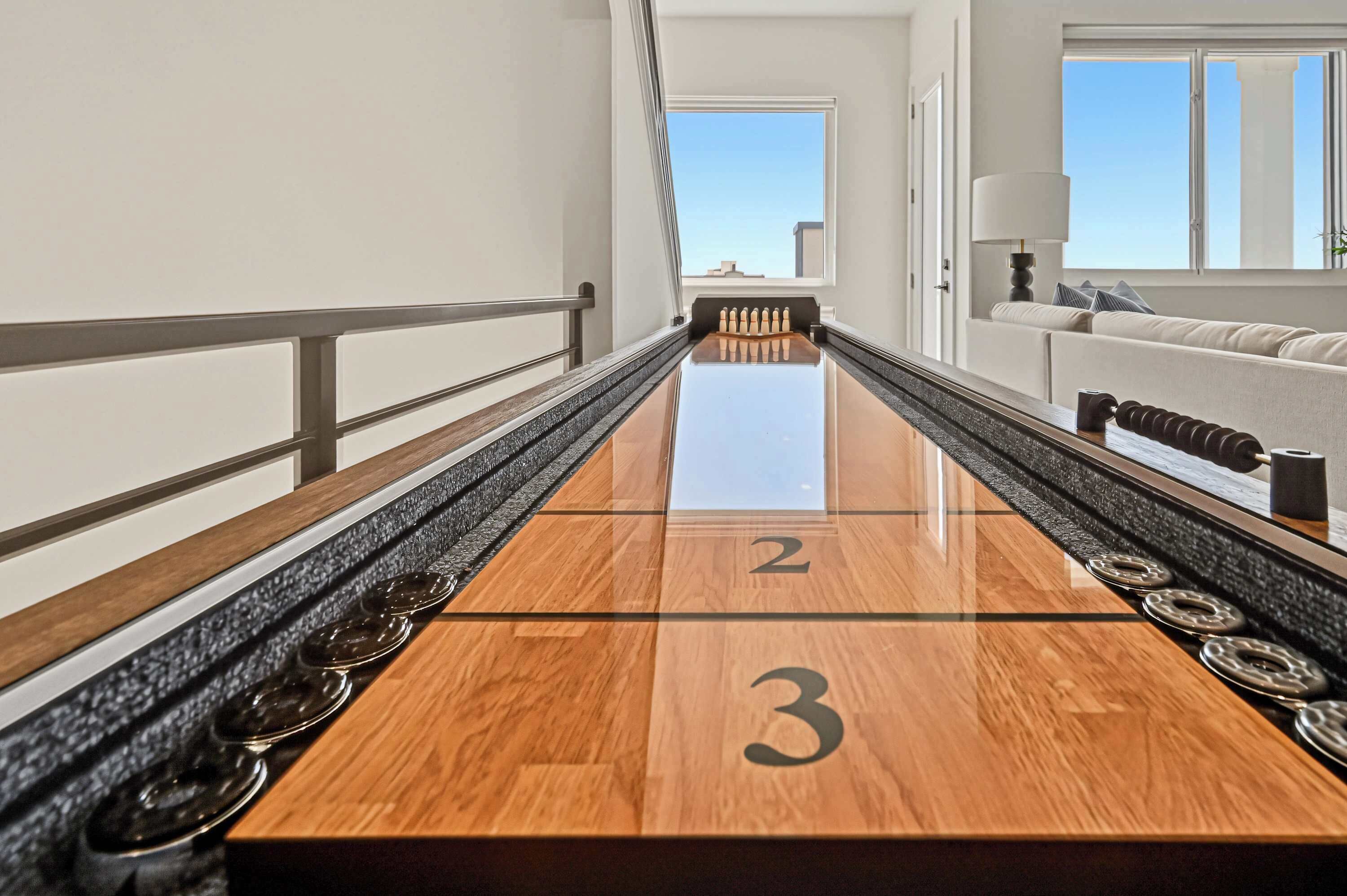 A shuffleboard table with numbers 2 and 3, a railing, and a view of a balcony with a sofa.