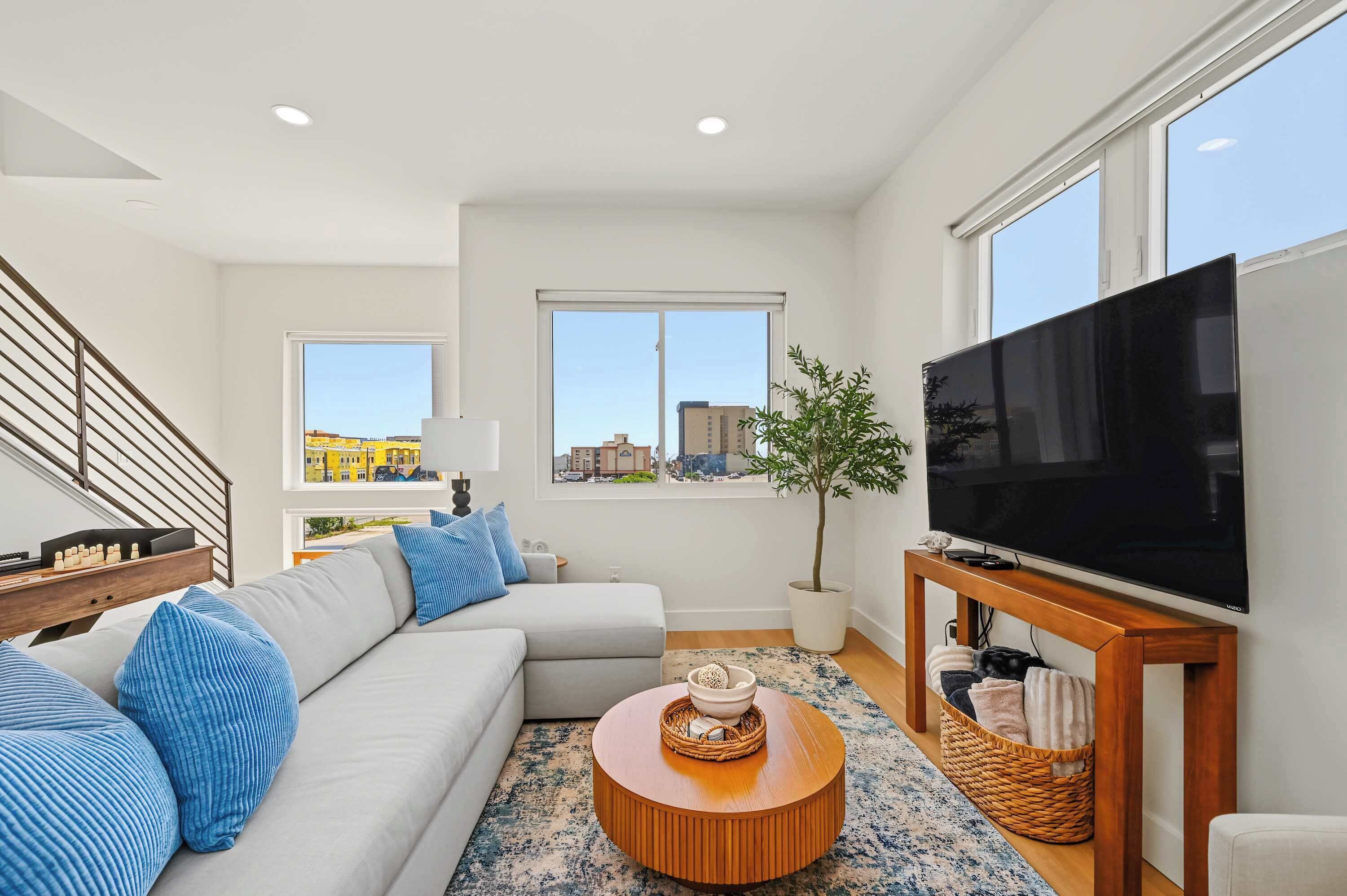 A modern living room with a sofa, a coffee table, a television, and a staircase.