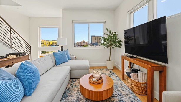A modern living room with a sofa, a coffee table, a television, and a staircase. - Coastal Loop Retreat | Rooftop Deck + Garage (Atlantic City)
