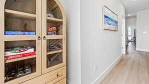 A wooden cabinet with drawers and shelves, a framed picture on the wall, and a hallway with a door at the end. - Coastal Loop Retreat | Rooftop Deck + Garage (Atlantic City)