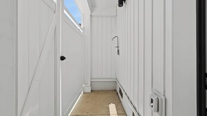 A narrow corridor with white walls and a concrete floor, leading to a door at the end. - Coastal Loop Retreat | Rooftop Deck + Garage (Atlantic City)