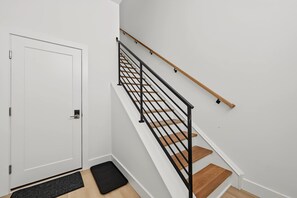 A staircase with a black metal railing and wooden steps, leading to a white door with a key lock. - The Coastal | Rooftop & Garage (Atlantic City)