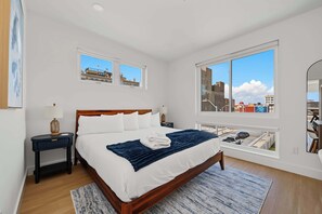 Ein Schlafzimmer mit einem großen Bett, zwei Nachttischen, einem Fenster mit Stadtblick und einem Spiegel an der Wand.