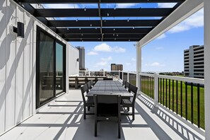A covered outdoor balcony with a dining table and chairs, overlooking a cityscape. - The Coastal | Rooftop & Garage (Atlantic City)