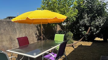 An outdoor dining area with a table and chairs, a yellow umbrella, and a garden backdrop.