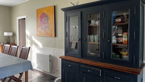 Un comedor con una mesa, sillas, un armario con puertas de vidrio y un cuadro en la pared.