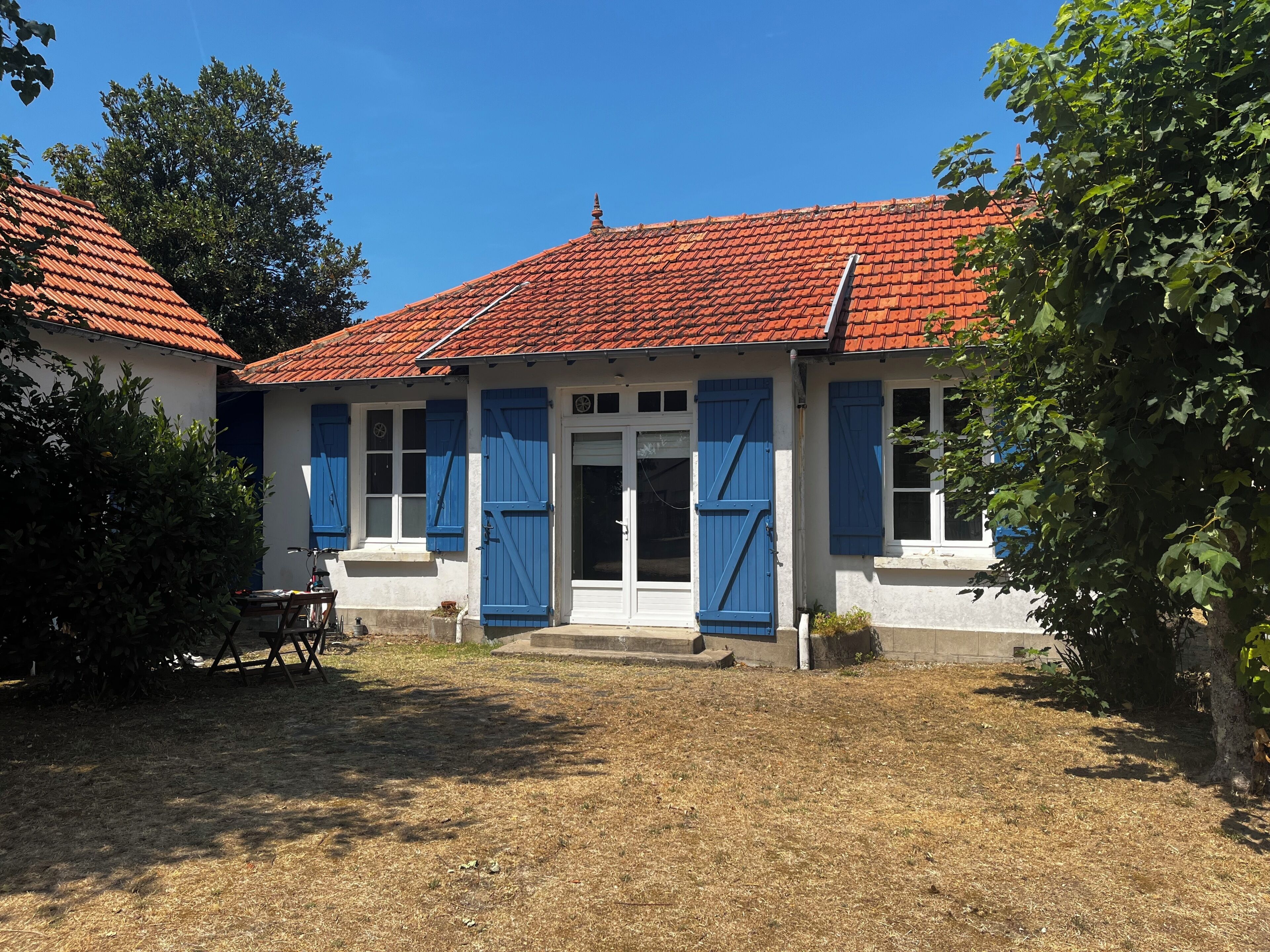 A two-story building with a red-tiled roof, white walls, and blue shutters.