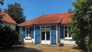 Un edificio de dos plantas con techo de tejas rojas, paredes blancas y contraventanas azules.