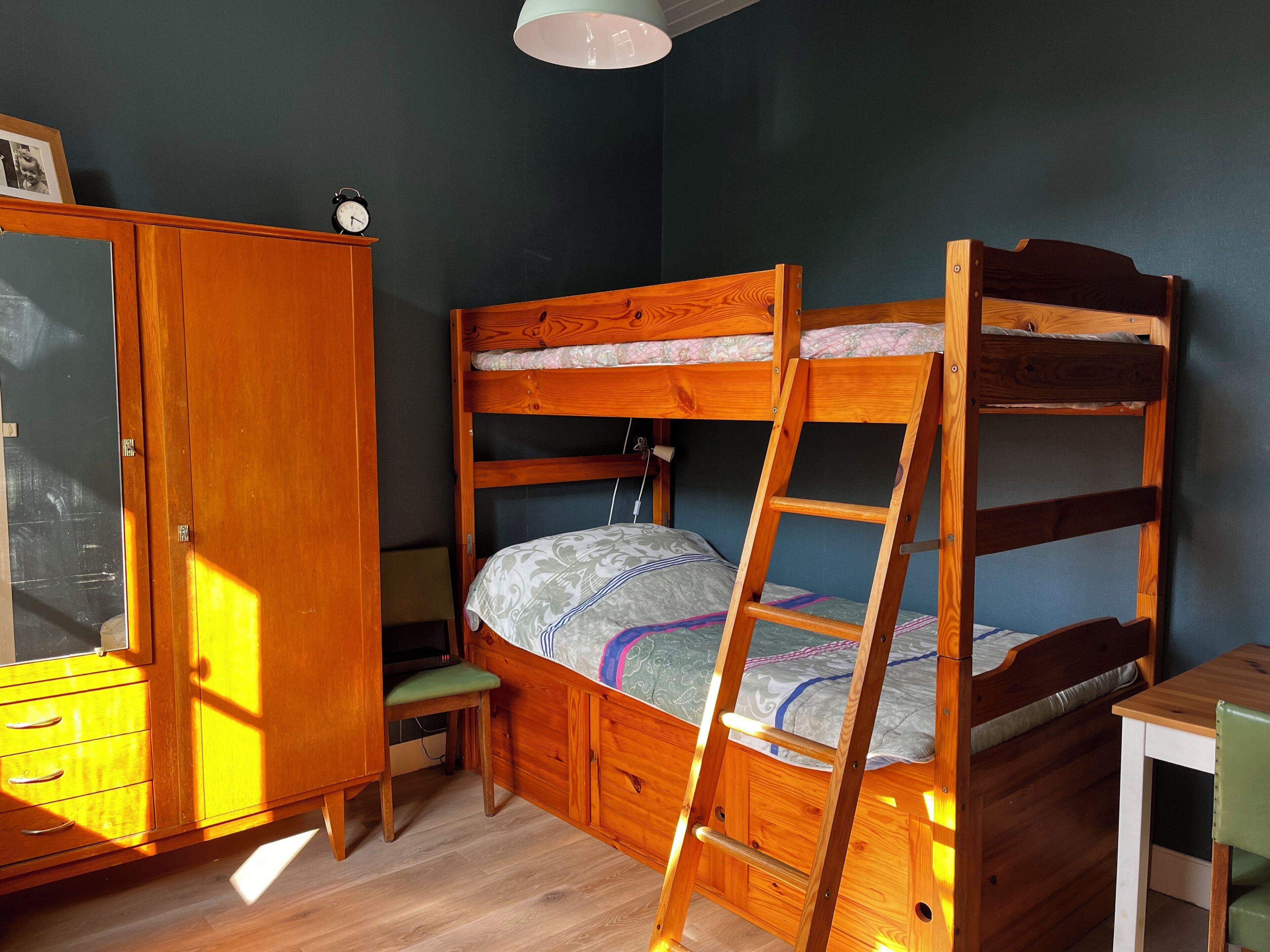 A bunk bed with a ladder, a wooden wardrobe, a desk, and a chair.