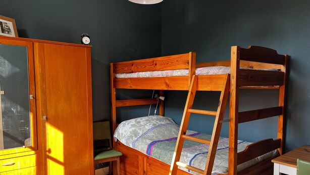 Una cama individual superpuesta con escalera, un armario de madera, un escritorio y una silla.