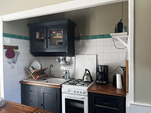 A kitchen with a stove, sink, cabinets, and a coffee maker.
