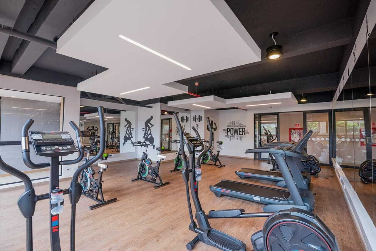 Une salle de sport moderne équipée de divers appareils de cardio, d’un grand miroir et d’œuvres d’art murales inspirantes.