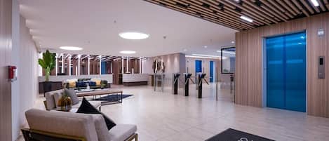 A modern lobby with a reception desk, seating area, and an elevator.