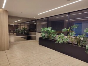 Un espace intérieur moderne avec un sol carrelé, des jardinières noires ornées de plantes vertes et une cloison de séparation en verre.