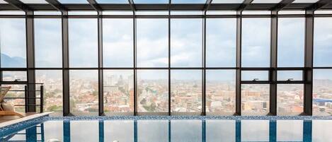 Une piscine à débordement intérieure offrant une vue sur la ville grâce à de grandes fenêtres.
