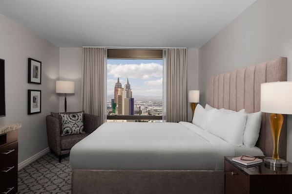 Ein Hotelzimmer mit einem großen Bett, zwei Nachttischlampen, einem Nachttisch, einem Sessel und Blick auf eine Stadtlandschaft durch ein großes Fenster.