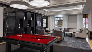 Un salon moderne doté d’une table de billard, de sièges confortables et d’une grande fenêtre offrant une vue sur la ville.