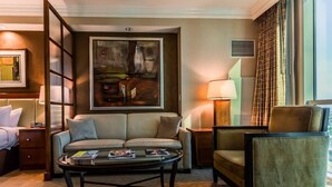 A hotel room with a sofa, armchair, and a coffee table. There is a painting on the wall and a window with curtains. - Free Valet Parking MGM Studio 1911 (Las Vegas)