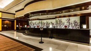 Ein moderner Hotel-Empfangsbereich mit einer gebogenen Rezeption, einer großen Wanddekoration und einem polierten Boden.