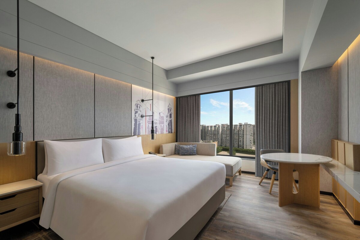 A modern hotel room with a large bed, a seating area, and a dining table.