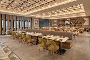 A modern restaurant with high ceilings, pendant lighting, and a variety of seating options including booths and tables.