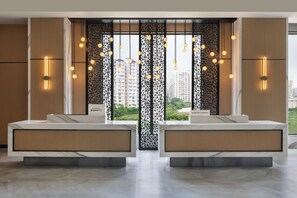 Un baño de hotel moderno con dos lavamanos, un separador decorativo y vistas a la ciudad.