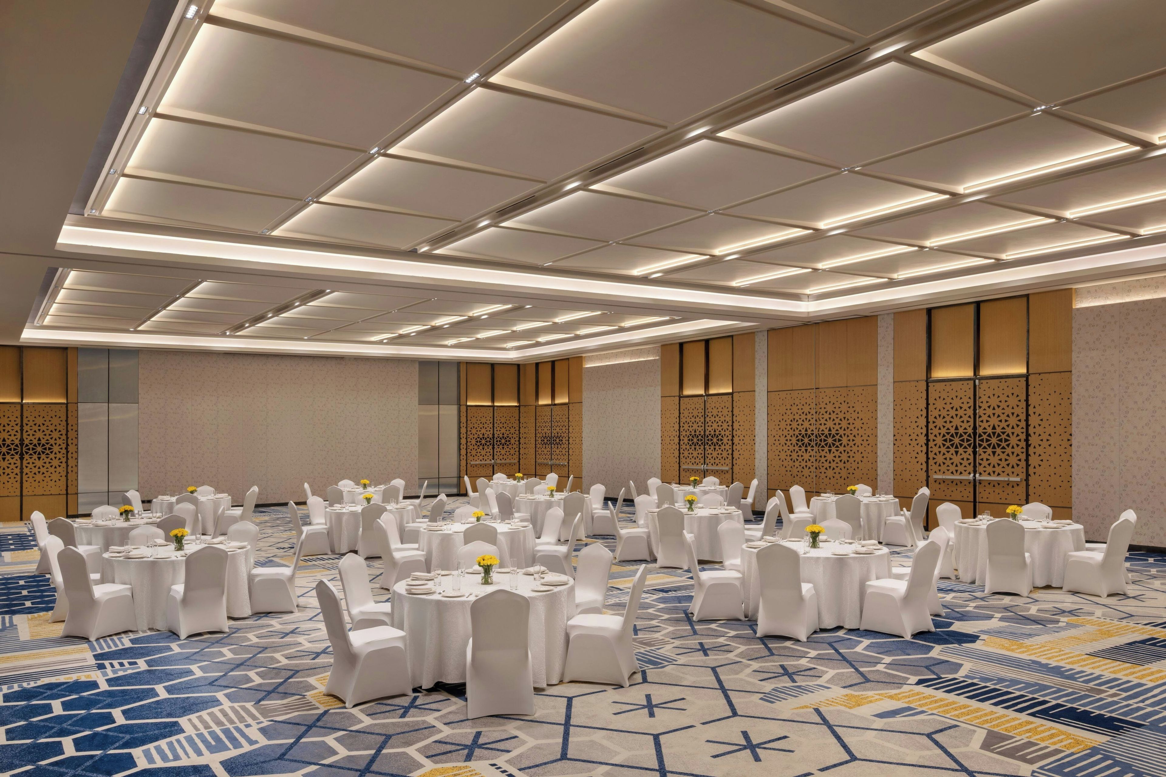 A banquet hall with round tables, white chairs, and patterned carpet.