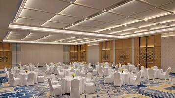 A banquet hall with round tables, white chairs, and patterned carpet.