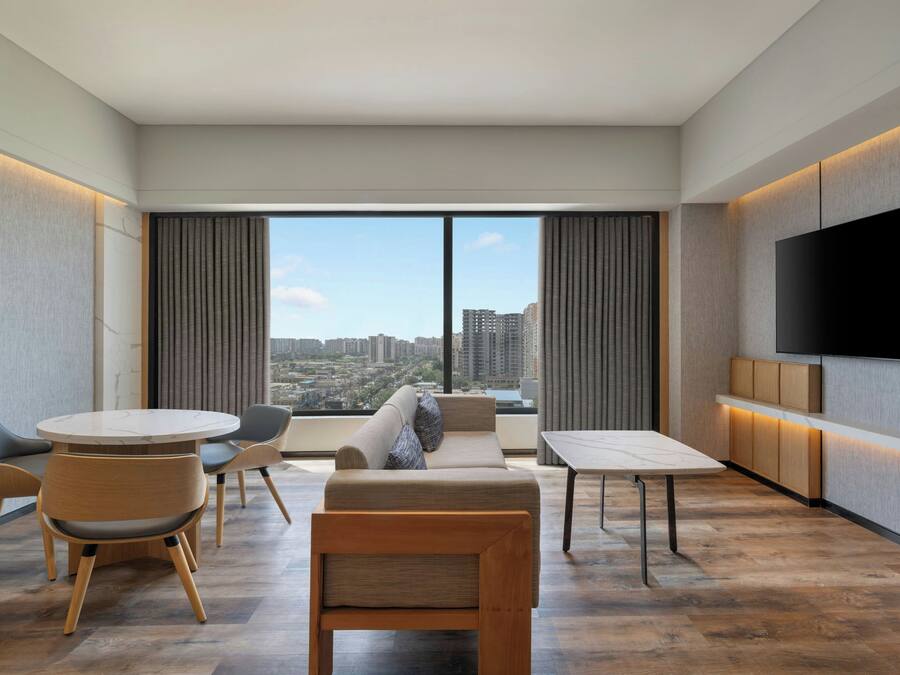 Une chambre d’hôtel moderne dotée d’une grande fenêtre, d’un téléviseur à écran plat, d’un canapé, d’une table à manger et d’une chaise.
