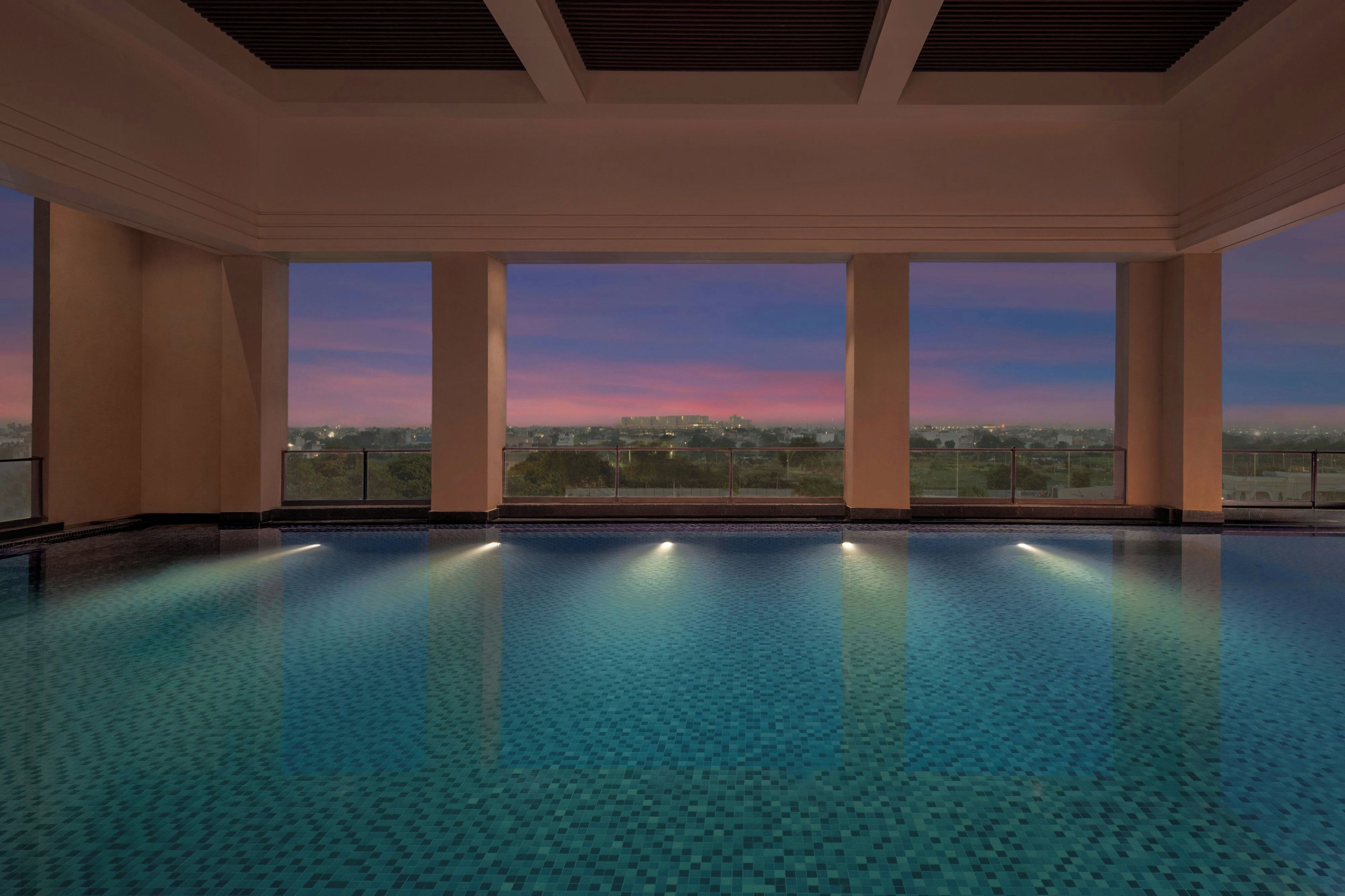 A large indoor swimming pool with a cityscape view at dusk.