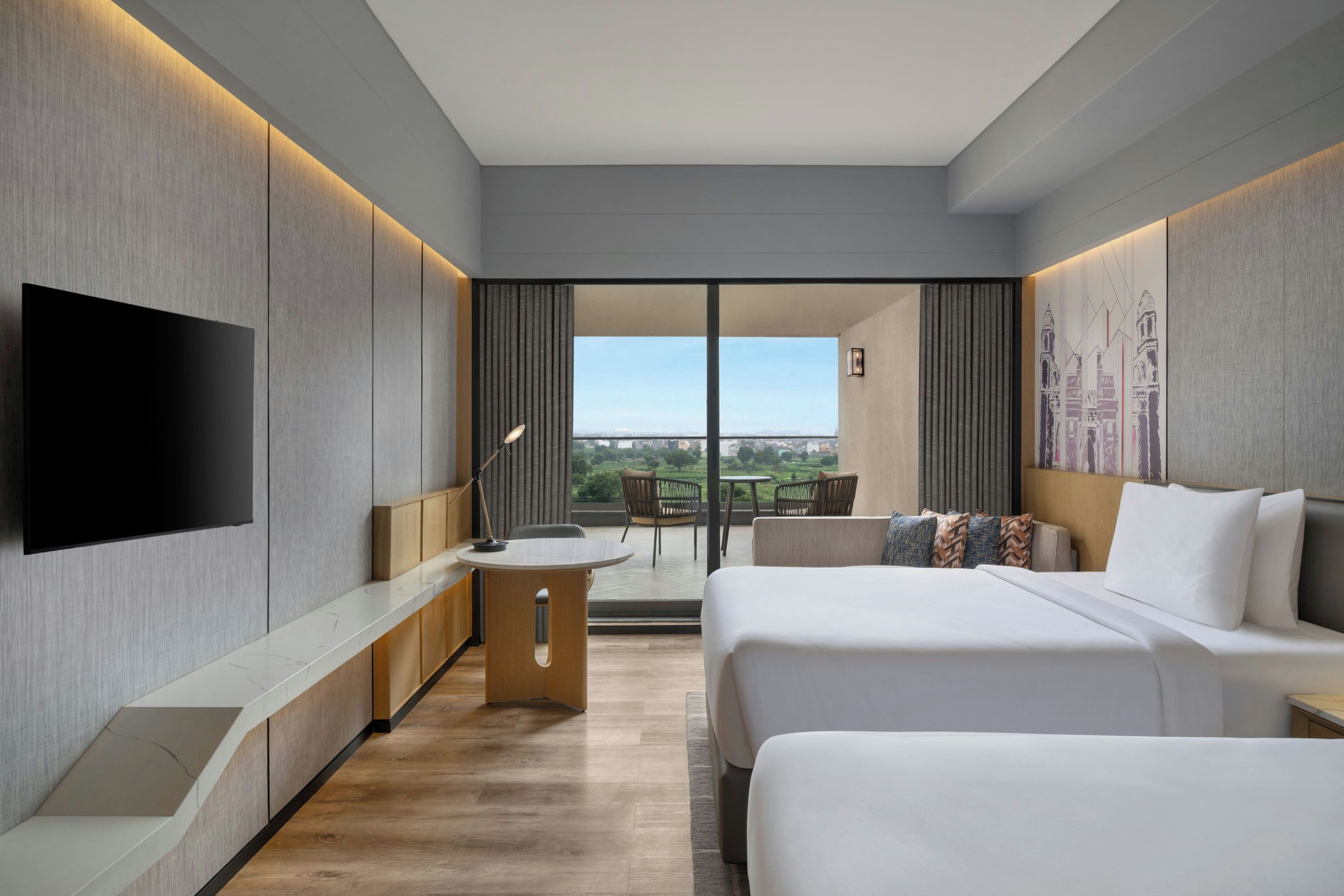 Een moderne hotelkamer met een flatscreen televisie, een bureau met lamp, een bed met witte lakens, en een balkon met uitzicht op de stad.