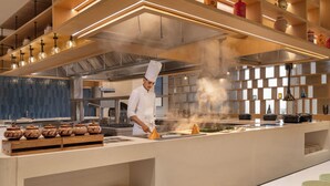 A modern kitchen with a chef preparing food, stainless steel appliances, and a variety of cooking utensils and ingredients. - Courtyard by Marriott Ghaziabad India (Ghaziabad)