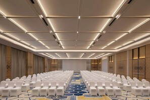 A conference room with rows of white chairs, a patterned carpet, and a ceiling with recessed lighting.