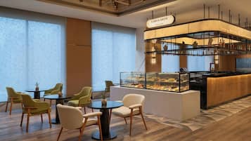 Un café moderno con barra, diferentes opciones de asientos y una vitrina con postres.