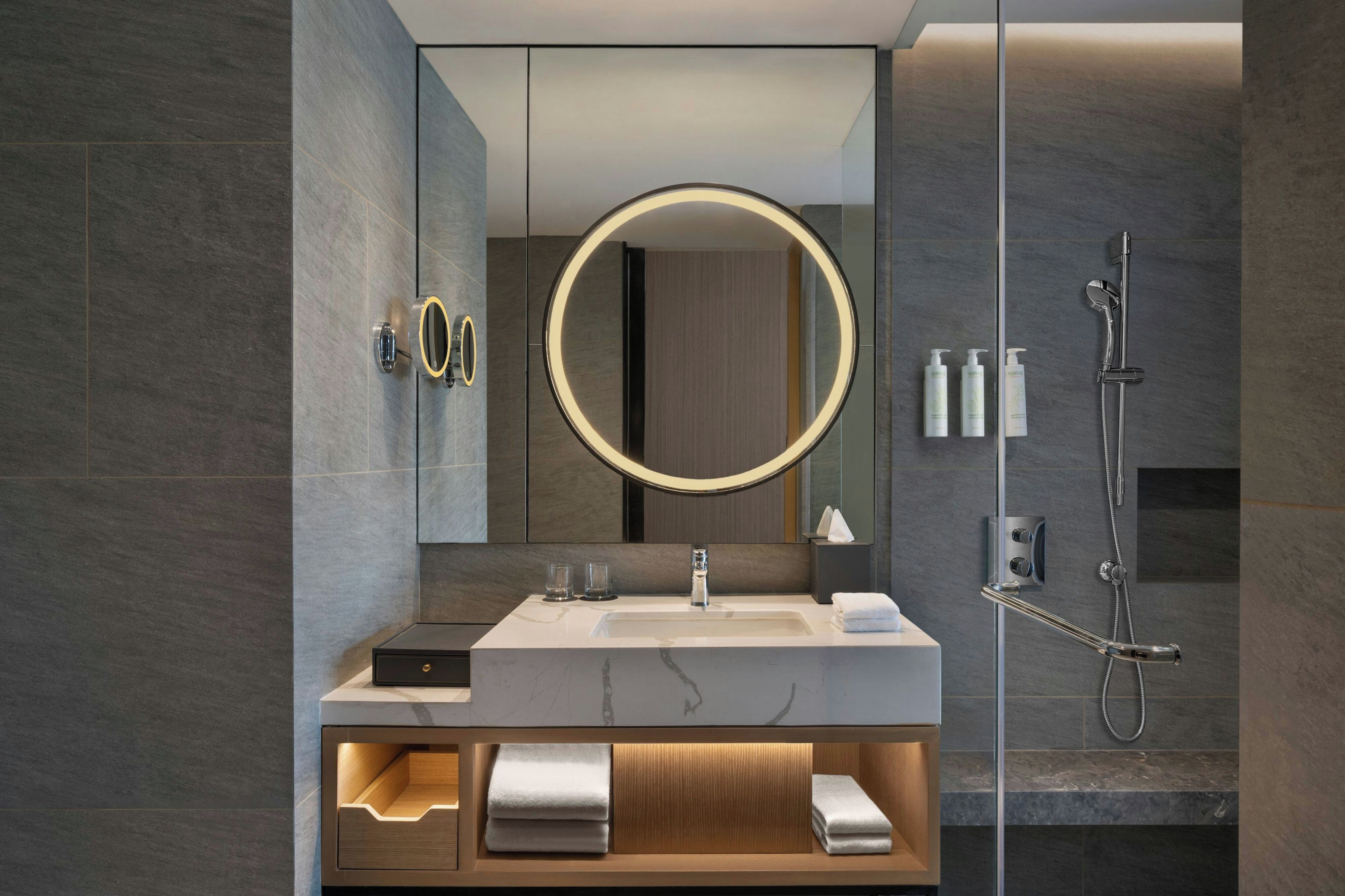 A modern bathroom with a large mirror, a handheld shower, and a vanity with a towel rack.