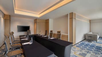 A conference room with a long table, chairs, a television, and a patterned carpet.