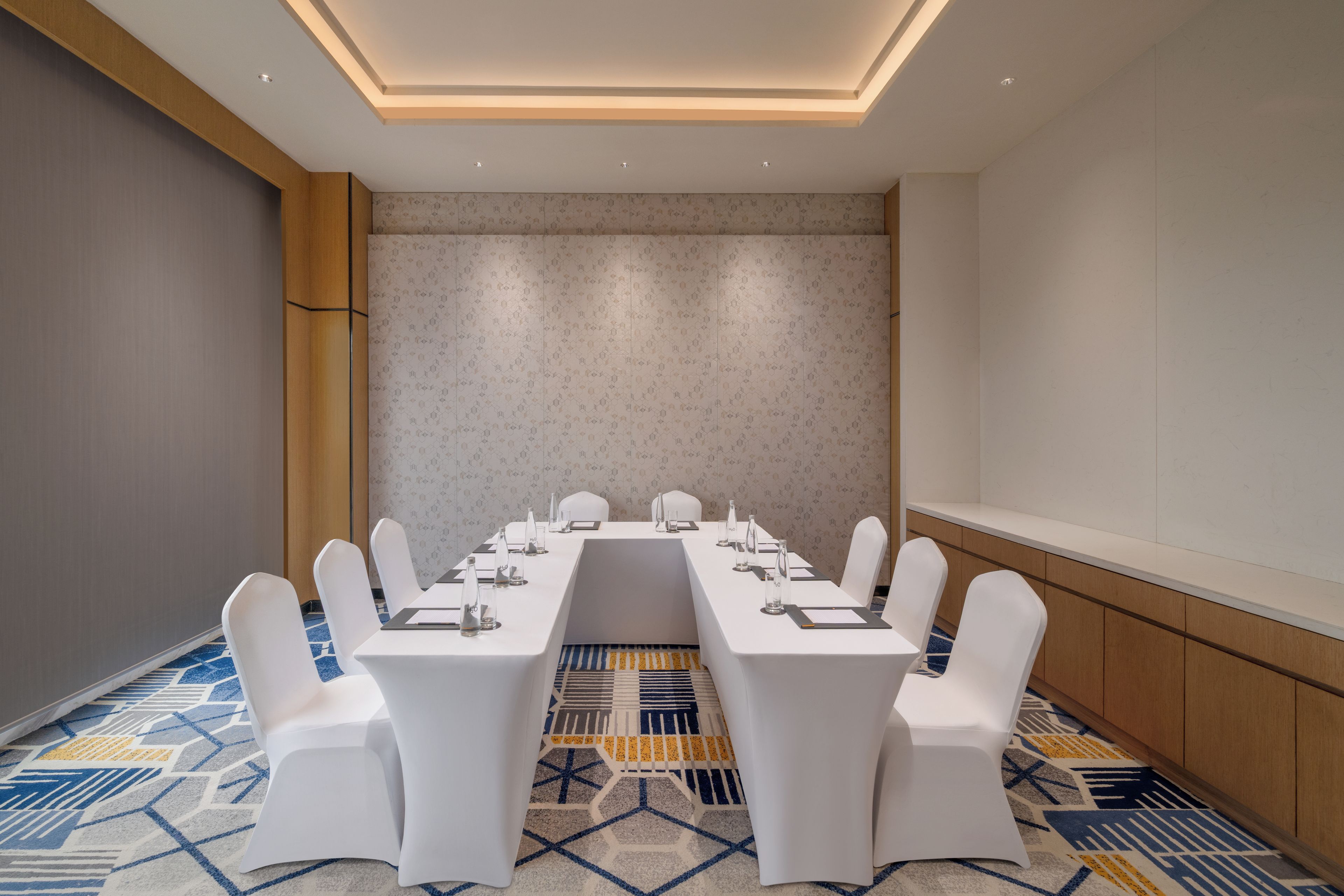 Una sala de conferencias con una larga mesa, sillas blancas y una alfombra estampada.