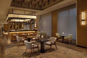 A modern bar area with a variety of liquor bottles, a seating area with round tables and chairs, and a large window providing a view.