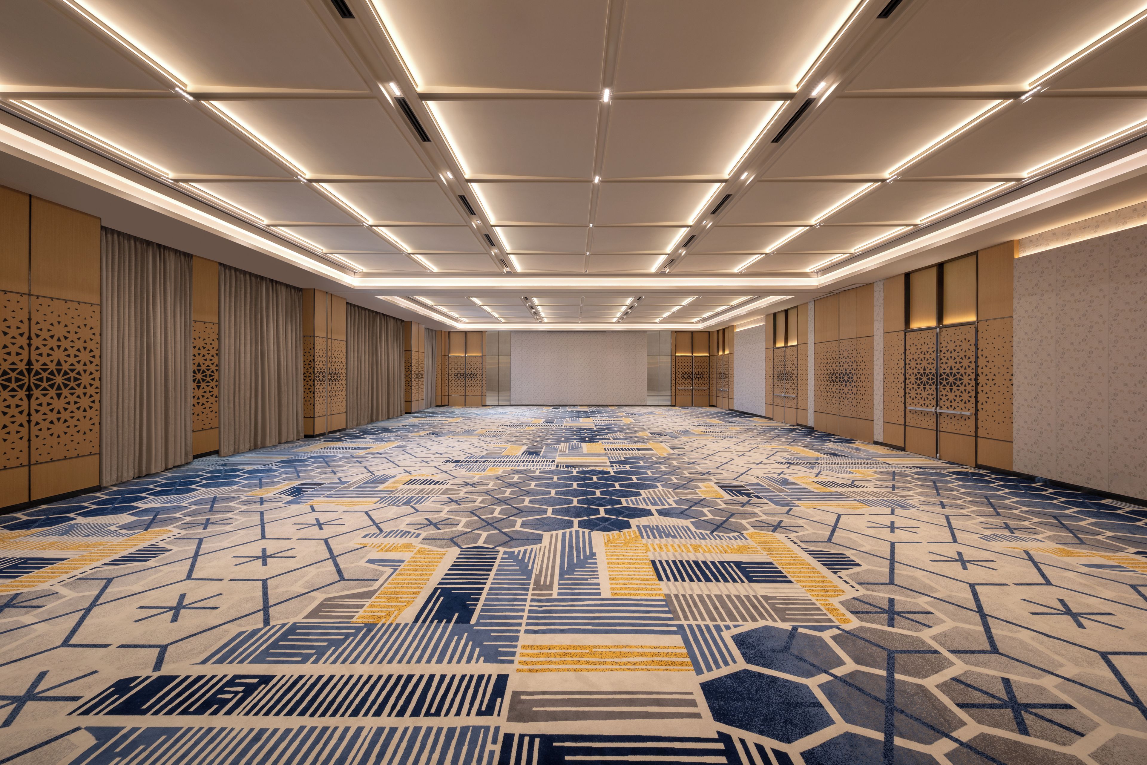 A spacious hotel lobby with a patterned carpet, recessed lighting, and traditional decor.