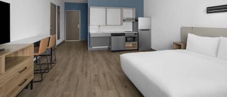 Una habitación de hotel con cama, televisión, escritorio con silla, kitchenette y baño.