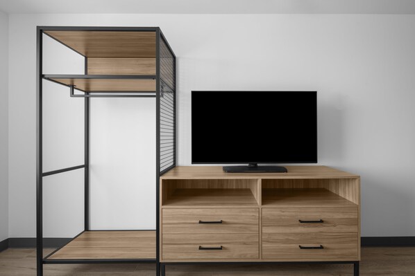 A room with a TV on a wooden cabinet, a metal shelving unit, and a white wall.